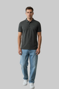 Man wearing a dark gray polo shirt and light blue jeans standing in a room with wooden furniture and decor.
